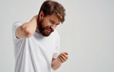 Man in white shirt touching neck with hand, experiencing neck pain